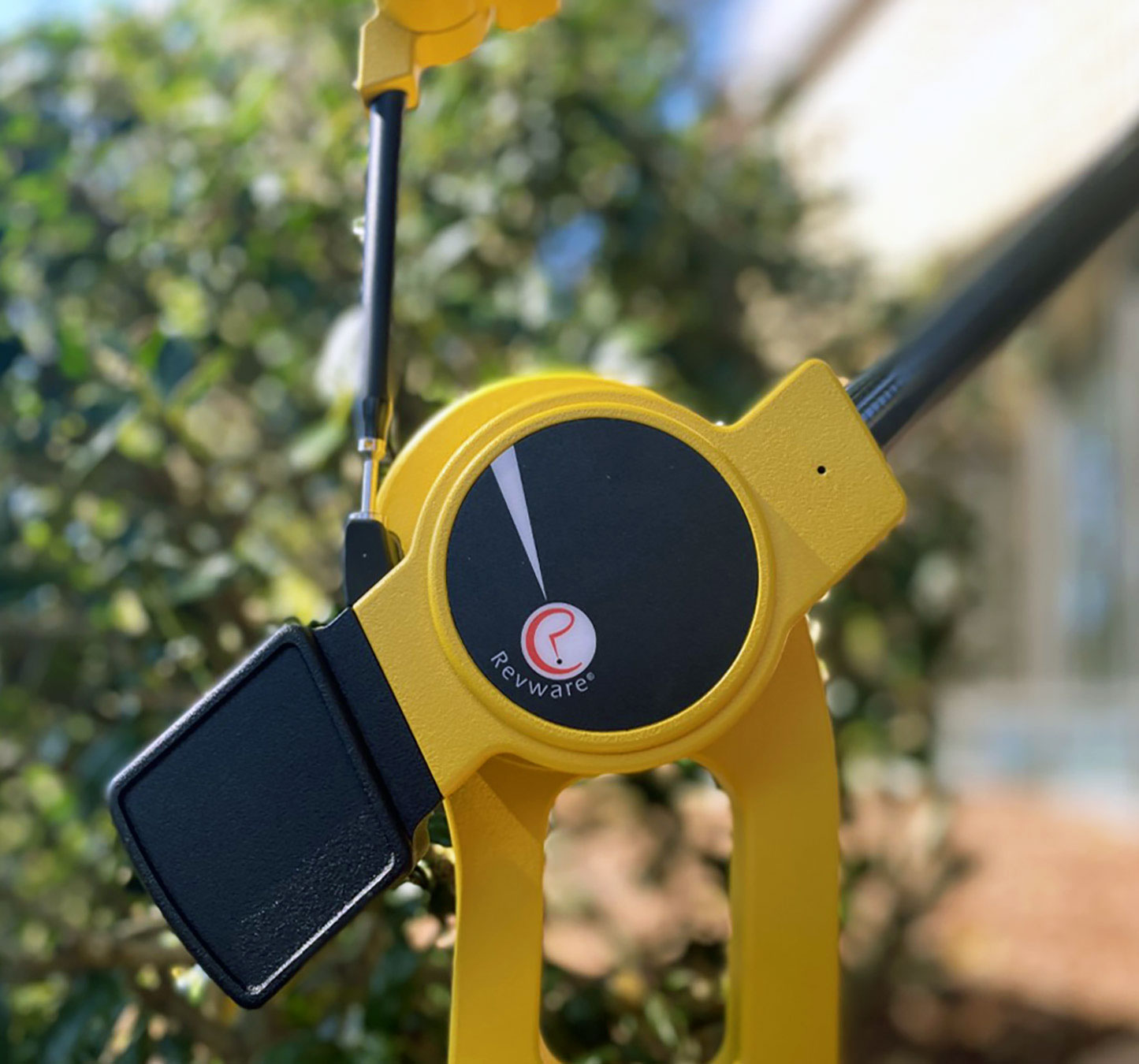 A closeup of a black and yellow digitizing arm showing the red and white revware logo, in the background a green bush.
