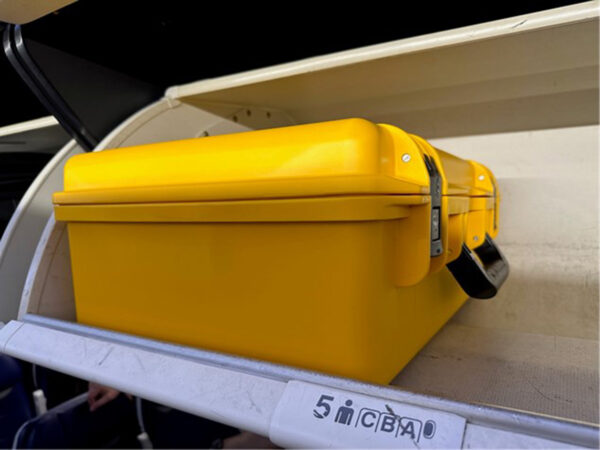 A yellow MicroScribe case sitting in an off-white airplane overhead compartment.
