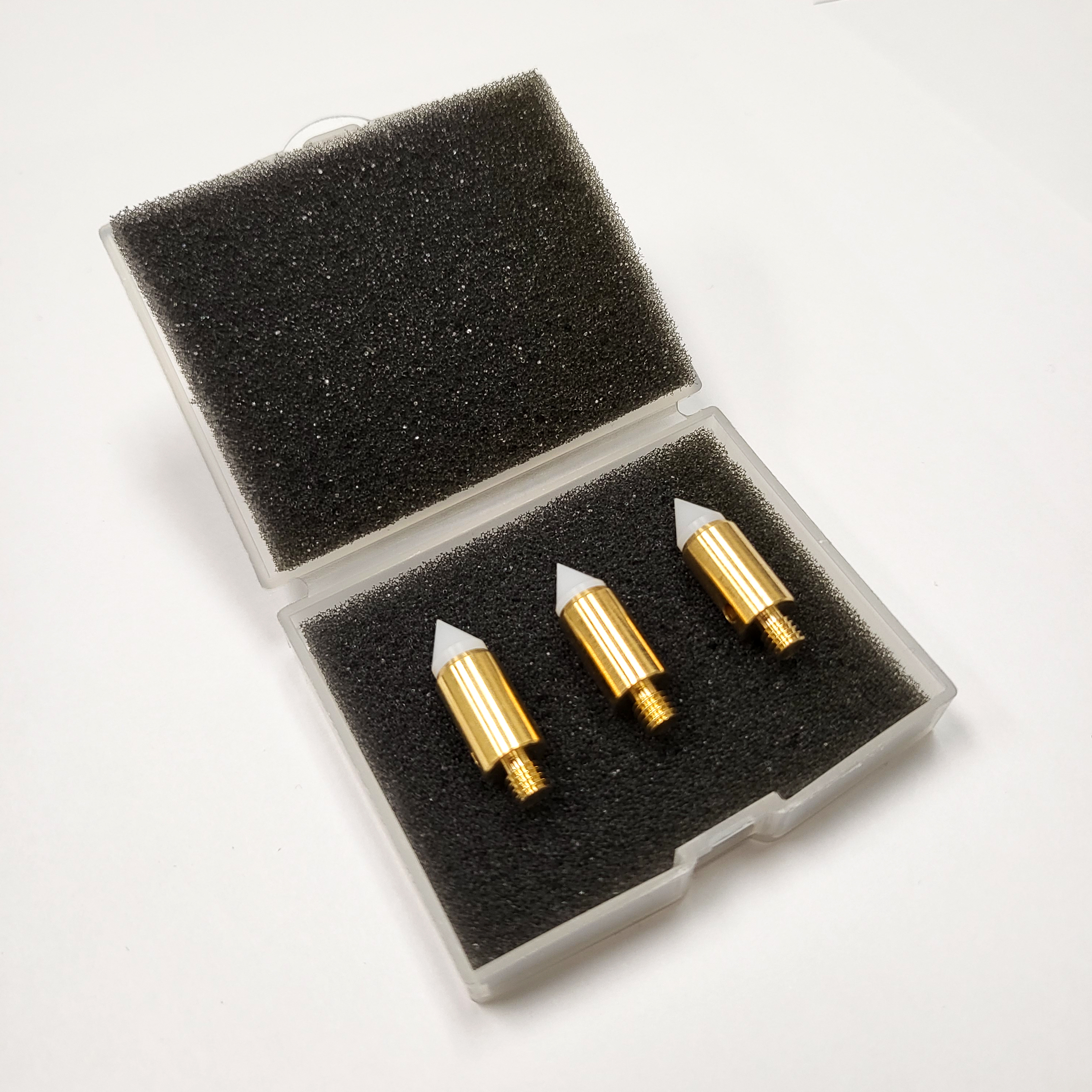 Three white and brass probe tips in a small clear box with the lid open and black foam inserts