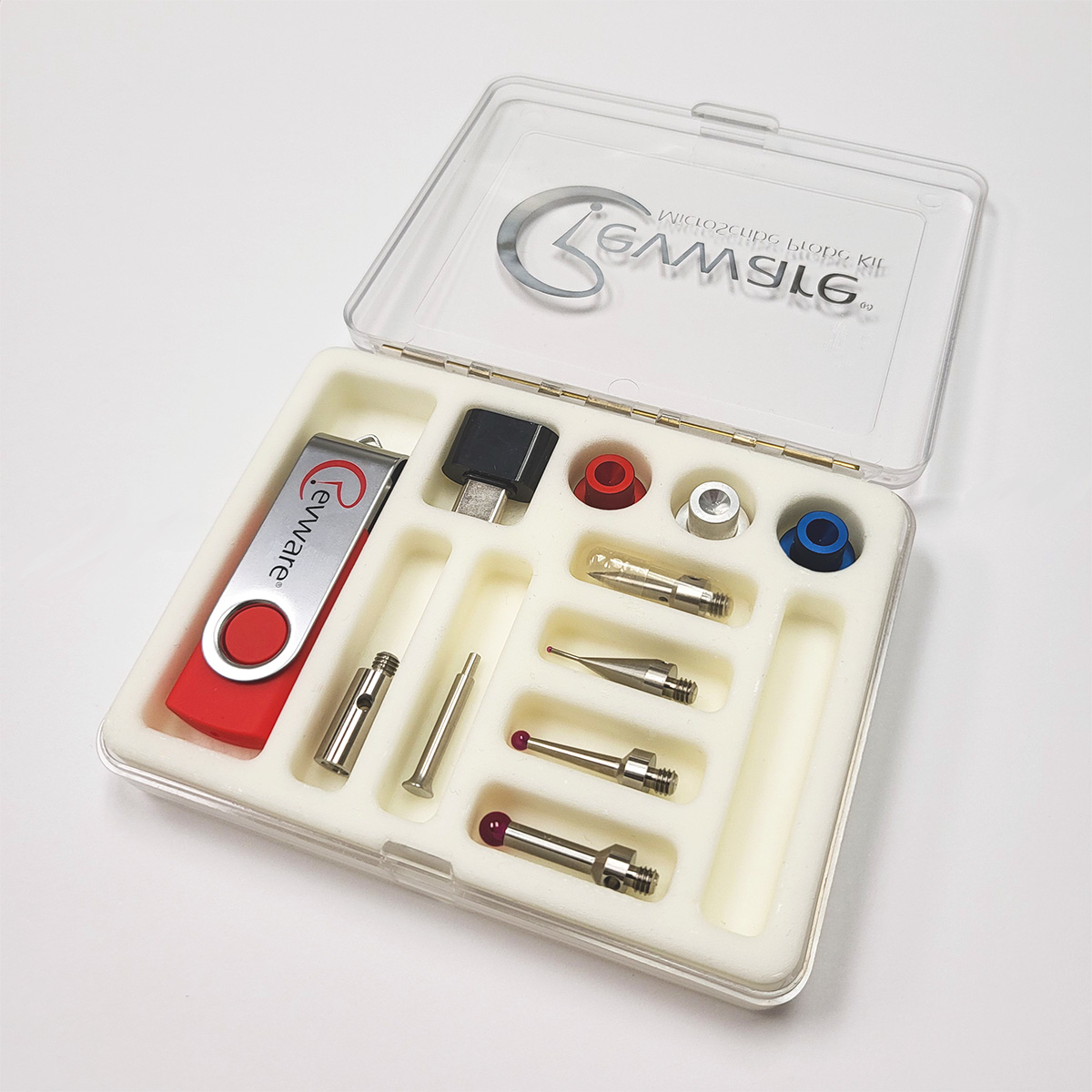 A small clear box on white background with the lid open, Revware logo on the lid, and white foam insert showing MicroScribe probe tips and USB drive.